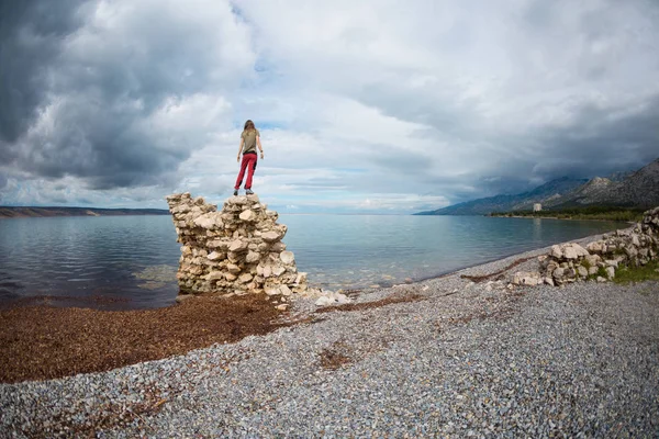 少女は石の山の上に立ち、海を見る. — ストック写真