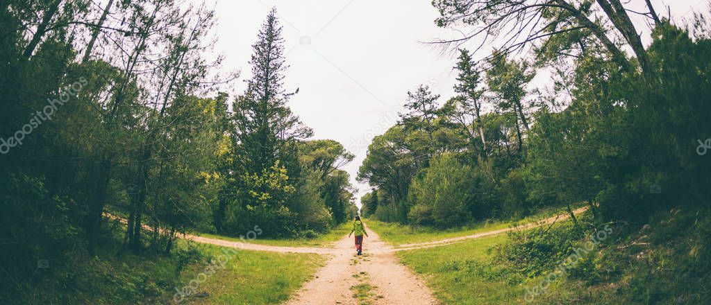 A woman stands at the crossroads of two forest roads.