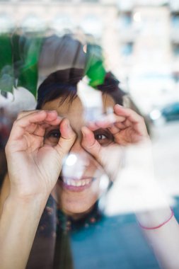 Gülümseyen kız bir kafede oturan ve pencereden dışarı bakıyor.