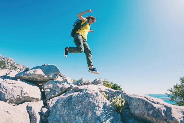 A woman with a backpack jumps over stones. — ストック写真