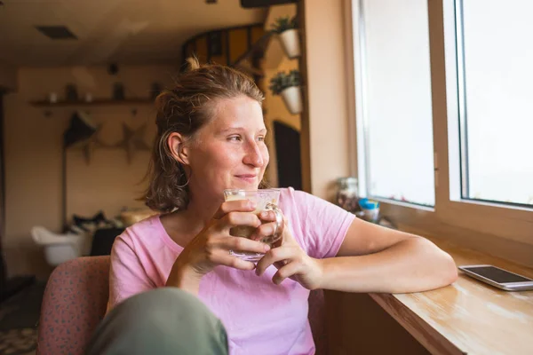 Una mujer está sentada cerca de la ventana y tomando café. . — Foto de Stock