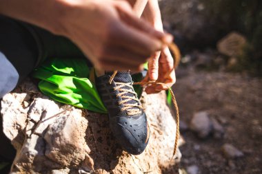 Kaya tırmanıcısı tırmanma ayakkabıları ve kravat bağcıkları giyer. Bir kız bir taşın üzerine oturur ve tırmanma ayakkabıları giyer. Rotayı aşmaya hazırlanıyorum. Kadın elleri yakın plan..