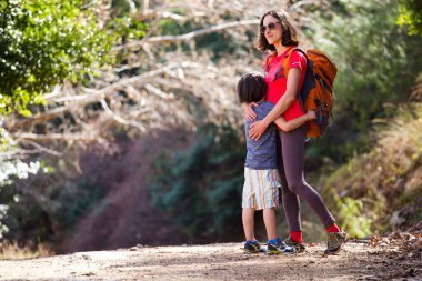 Parkta bir çocuk annesine sarılıyor. Sırt çantalı bir kadın oğluyla ormanda yürüyor. Çocuk annesiyle seyahat ediyor. Annemin kucaklaması..