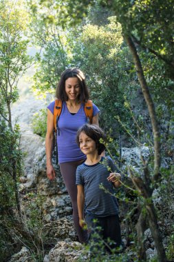 Bir kadın oğluyla ormanda yürür, annesiyle yürüyüşe çıkar, sırt çantalı bir çocuk parka gider, çocuklarla seyahat eder, çocuk annesinin elini tutar, dağ yolu, Anneler Günü..