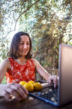 Kırmızı elbiseli bir kız, ahşap bir evin verandasında internet üzerinden akrabalarıyla iletişim kuruyor, bir yazlık evin terasında işten dinlenen bir kadın, dizüstü bilgisayar ve masada limonlar..