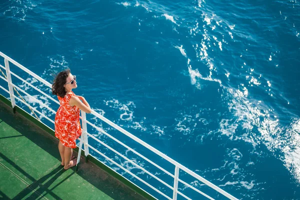 A woman is sailing on a cruise ship, a girl is standing near the fence on a ship and looking at the sea, view from above, traveling by ferry, a brunette in a summer dress admires the ocean.