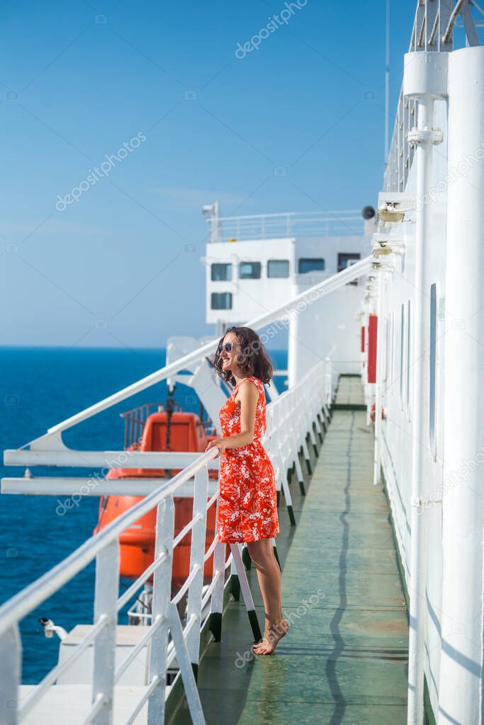 A woman is sailing on a cruise ship, a girl is standing near the fence on a ship and looking at the sea, traveling by ferry, a brunette in a summer dress admires the ocean.