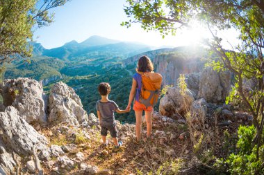 Oğlan ve annesi dağın tepesinde duruyorlar, bir kadın çocukla seyahat ediyor, çocuk annesiyle dağlara bakıyor, sırt çantalarıyla seyahat ediyor, yürüyüş yapıyor ve çocuklarla tırmanıyor..