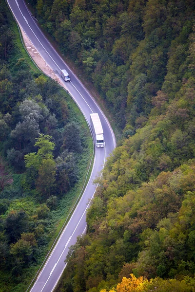 Highway through the forest aerial view. Asphalt road in the mountains. Transport connection. Cars on the road. The path through the forest.