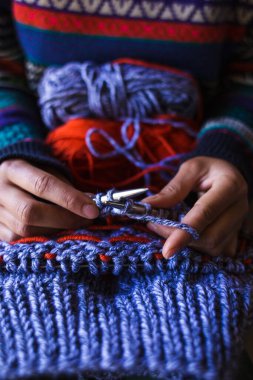Kadın yün iplikten bir şapka örüyor. Kadın eli, yakın plan. El yapımı. Renkli iplik ve örgü iğneleri.