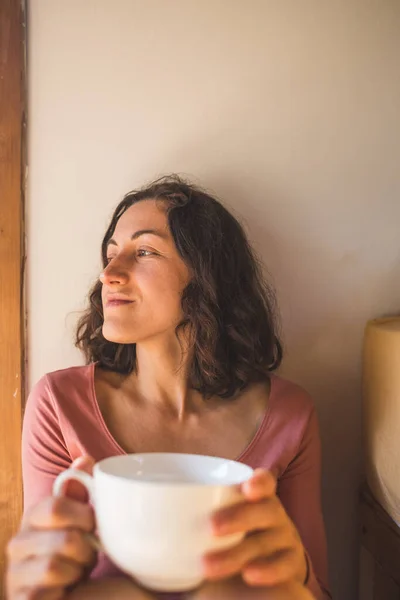 A woman is enjoying morning coffee at home, Portrait of a smiling brunette with a cup of morning drink, Girl is drinking tea.