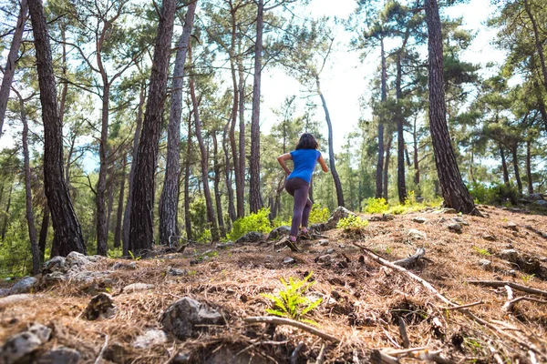 A woman runs along a mountain trail. Runner is training in the forest. Girl jogging in the park. Skyrunning.