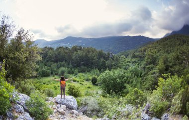 Sırt çantalı bir kadın, elleri havada bir dağın tepesinde durur ve bir dağ vadisinin güzelliğine hayran kalır, güzel yerlere seyahat eder, hedefe ulaşır, güzel manzaraya ulaşır..