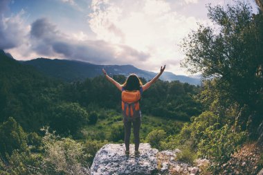 Sırt çantalı bir kadın, elleri havada bir dağın tepesinde durur ve bir dağ vadisinin güzelliğine hayran kalır, güzel yerlere seyahat eder, hedefe ulaşır, güzel manzaraya ulaşır..