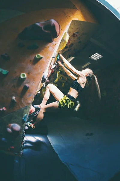 少女は体育館で訓練を受けている ロッククライマーは人工の壁で訓練してる 壁を登る ジムでボーリング 強い女性はスポーツのために行く — ストック写真