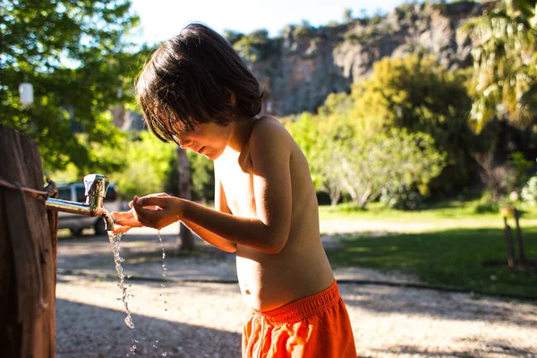 Tired of the heat, the child washes his body with water from a tap in the courtyard of the house. The boy is doused with tap water. Hot Summer. Spray. Vacation in the village.