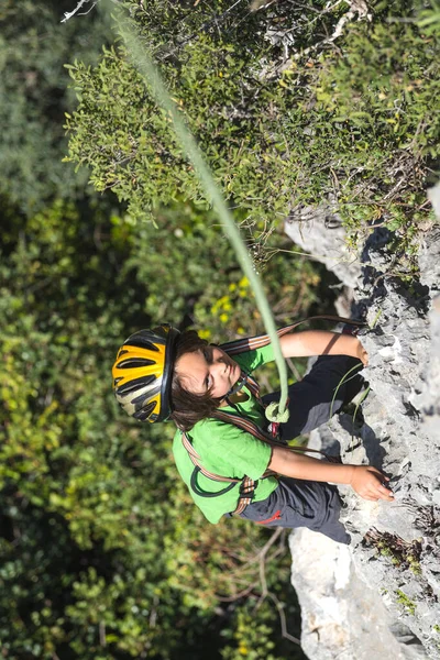子供は自然の地形に登っています ヘルメットを被った少年が山を背景に岩を登る 趣味は アスレチックキッズの列車が強いです ロッククライミングの安全性 — ストック写真