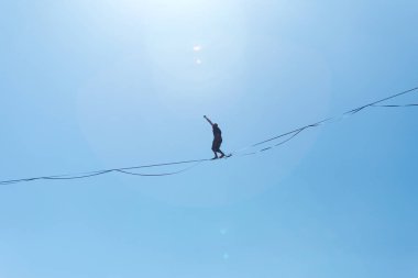 Bir adam mavi gökyüzüne karşı Highline boyunca yürüyor. Highliner askı takıyor. İp cambazı. Bir adam dengeyi yakalar..
