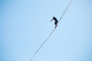 Bir adam mavi gökyüzüne karşı Highline boyunca yürüyor. Highliner askı takıyor. İp cambazı. Bir adam dengeyi yakalar..