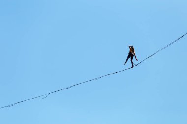 Bir adam mavi gökyüzüne karşı Highline boyunca yürüyor. Highliner askı takıyor. İp cambazı. Bir adam dengeyi yakalar..