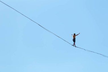 Bir adam mavi gökyüzüne karşı Highline boyunca yürüyor. Highliner askı takıyor. İp cambazı. Bir adam dengeyi yakalar..