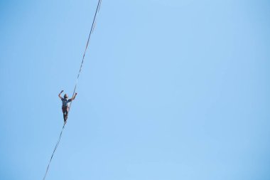 Bir adam mavi gökyüzüne karşı Highline boyunca yürüyor. Highliner askı takıyor. İp cambazı. Bir adam dengeyi yakalar..
