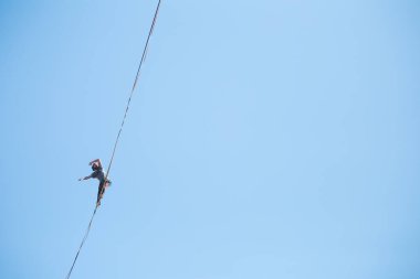 Bir adam mavi gökyüzüne karşı Highline boyunca yürüyor. Highliner askı takıyor. İp cambazı. Bir adam dengeyi yakalar..