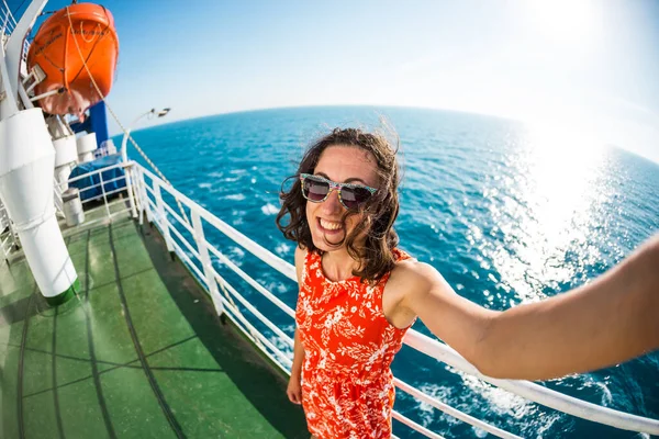 A woman is sailing on a cruise ship, a girl is standing near the fence on a ship against the sea and makes selfie, traveling by ferry, a brunette in a summer dress admires the ocean.