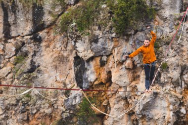Bir adam gerilmiş askı boyunca yürüyor. Dağlarda yüksek bir yer. İnsan dengeyi yakalar. Doğada bir ip cambazının performansı. Dağların arka planındaki dağcı..