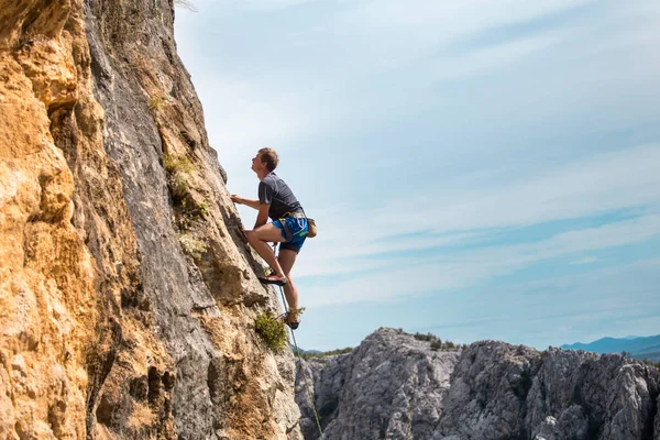 山や海の背景にロッククライマー 男が岩の上を登る 自然の中でトレーニング 積極的なライフスタイル 趣味は スポーツにおける強みと耐久性 — ストック写真