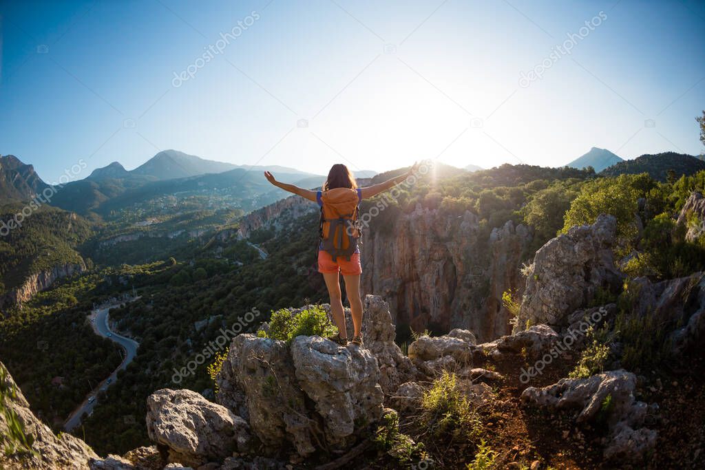 A woman with a backpack stands on top of a mountain with her hands up and admires the beauty of a valley, The girl travels to beautiful places, Reaching the goal, Beautiful landscape of Turkey.