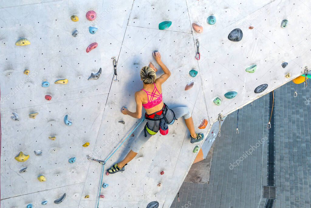 A woman climbs a climbing wall, a climber is training on artificial terrain, rock climbing in the city, a strong girl, sports in the city, safety in extreme sports.