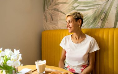 Kafede bir kadın oturuyor, bardakta bir kapuçino, sabah kahvesi, kısa saçlı sarışın bir kız..