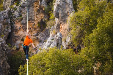 Bir adam gerilmiş askı boyunca yürüyor. Dağlarda yüksek bir yer. İnsan dengeyi yakalar. Doğada bir ip cambazının performansı. Dağların arka planındaki dağcı..