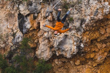 Bir adam gerilmiş askı boyunca yürüyor. Dağlarda yüksek bir yer. Adam dengesini kaybetti. Doğada bir ip cambazının performansı. İpe asılmış bir dağcı. Sonbahar sporcusu.