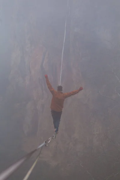 一个人在雾中沿着一条伸展的吊带走着 在山中高耸 人保持平衡 大自然中走钢丝的人的表现 雷云背景下的高音 — 图库照片