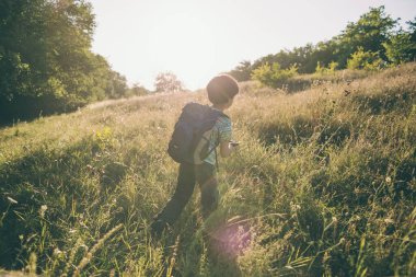 Sırt çantalı bir çocuk çayırda yürüyor, bir çocuk vahşi hayatı keşfediyor, bir çocuk ağaçların arasında tek başına duruyor, bir çocuğun portresi..