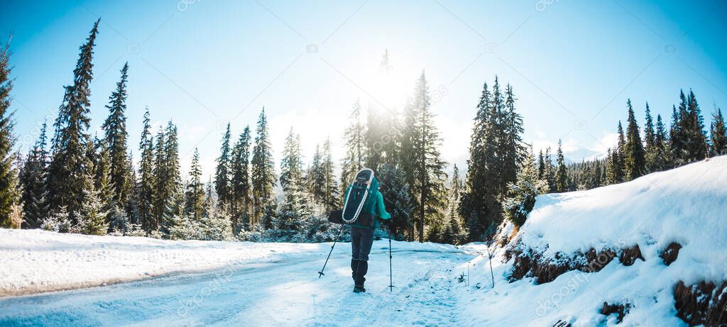 Woman with backpack and snowshoes in the winter mountains. Travel to scenic places. Blonde with trekking sticks. A tourist walks through a snowy forest. Girl walks along the path.