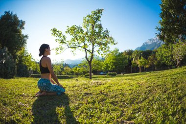 Kız yeşil çimlerde, yeşil ağaçların ve dağların arka planında yoga yapıyor, gün batımında asma dansı yapıyor, doğada meditasyon yapıyor, dengenin gelişmesi için egzersiz yapıyor..