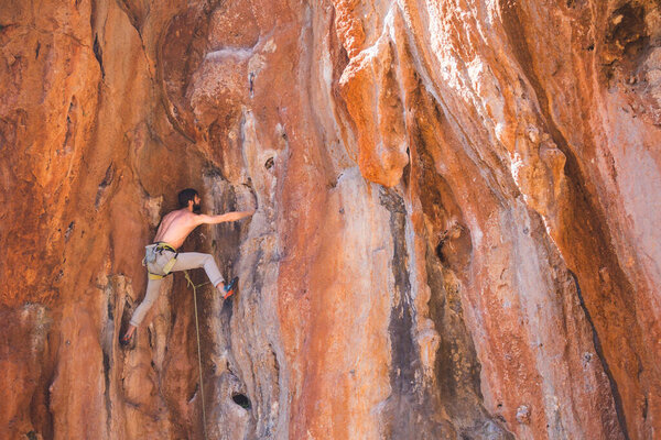 A strong man climbs a cliff. Climber overcomes a difficult climbing route on a natural terrain. Rock climbing in Turkey. Beautiful orange rock.