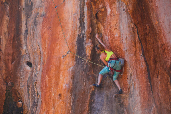 A girl climbs a rock. The athlete trains in nature. Woman overcomes difficult climbing route. Strong climber. Extreme hobby. Rock climbing in Turkey.