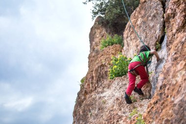 Çocuk doğal bir araziye tırmanıyor. Bir çocuk dağların arka planında bir kayaya tırmanır. Olağanüstü bir hobi. Atletik çocuk güçlü olmayı öğrenir. Kaya tırmanışı güvenli.