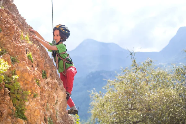 子供は自然の地形に登っています 少年は山を背景に岩に登る 趣味は アスレチックキッズの列車が強いです ロッククライミングの安全性 — ストック写真