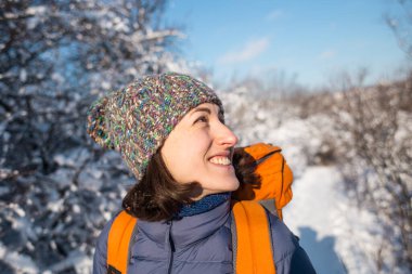 Örgü şapkalı bir kızın portresi karlı bir ormanın arka planında sırt çantasıyla gülümseyen bir kadın kış yürüyüşündeki bir kadın, dağlara tırmanan bir kış..