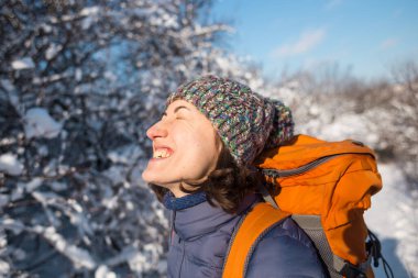 Örgü şapkalı bir kızın portresi karlı bir ormanın arka planında sırt çantasıyla gülümseyen bir kadın kış yürüyüşündeki bir kadın, dağlara tırmanan bir kış..