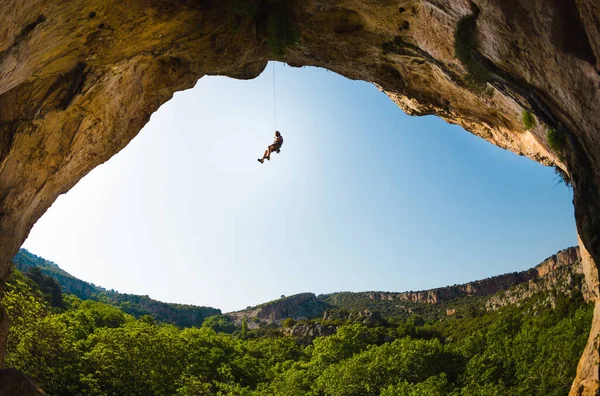 Rock climber hanging on a rope, A man climbs a rock in the shape of an arch, The man climbs in the cave, Climbing rope for belaying, Rock climbing in Turkey.