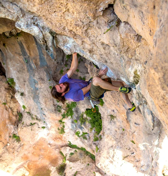 A strong man climbs a cliff, Climber overcomes a difficult climbing route on a natural terrain, Rock climbing in Turkey, Beautiful orange rock.