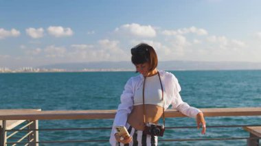 Kadın blogcu sosyal ağlar için içerik çekiyor ve kameraya el sallıyor. Gülümseyen turist cep telefonuyla selfie çekiyor.