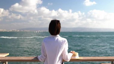 Çekici bir kadının yakın plan portresi, gülümseyen, esmer, kendine güvenen, deniz kenarında duran. Kız gülümser ve kameraya bakar.