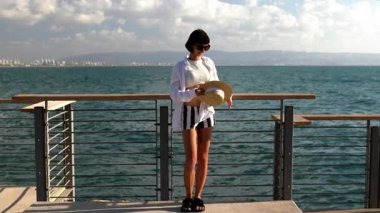 Sakin ve sakin bir kadın hasır bir şapka takıp okyanusa bakıyor. Deniz kenarında yaz tatili. Deniz kenarında özgürlük ve rahatlama.